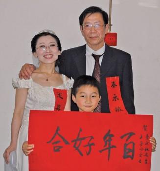 Qin Yongming och Wang Xifeng vid deras bröllop den 13 maj i Wuhan. Wangs 12-årige son håller ett plakat med texten ”ett bra äktenskap varar i hundra år”. (Foto från Wang Xifeng). 