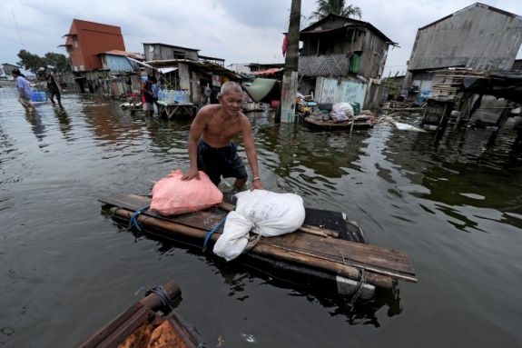 En man för en hemmabygd flotte lastad med tillhörigheter genom de översvämmade vattenmassorna, orsakade av en tyfon i Malabon, Manila den 21 juni. (Foto: Noel Celis/AFP/Getty Images)