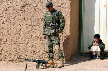 Ett afghanskt barn tittar på en soldat ur den afghanska nationella armén (ANA) som står på vakt i byn Qari Saheb i Nad-e Ali-distriktet i provinsen Helmand under andra dagen av den gemensamma operationen 'Moshtarak' den 14 februari. Nato har bekräftat att två amerikanska raketer träffade ett hus och dödade 12 civila. Koalitionsstyrkor uppger att de har dödat minst 20 talibaner, och rapporterar tre dödade i egna trupper. (Foto: Massoud Hossaini / AFP / Getty Images)