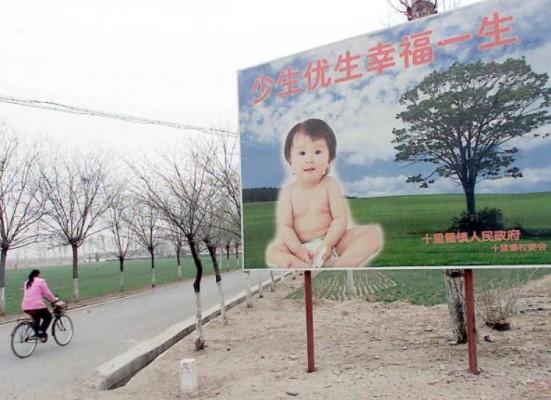 En kvinna cyklar förbi en reklamskylt, där par uppmuntras till att ha bara ett barn, längs en väg som leder till ett samhälle i förorten till Peking, den 25 mars 2001. En partitjänsteman har nyligen föreslagit att man går över till tvåbarnspolitik i vissa regioner. (Foto: Goh Chai Hin/AFP/Getty Images)