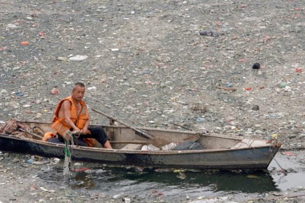 En kinesisk arbetare försöker rensa bort sopor från en kanal i Peking, den 2 juli 2007. Enligt en rapport från norra Kinas miljöövervakningscentrum har prov tagna från 37 floder i Pekingområdet föroreningsnivåer som är högre än vad som anses säkert. (Teh Eng Koon/AFP/Getty Images)