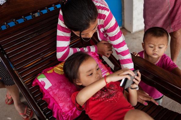 5-åriga Hak Kimlang spelar spel på sin mobiltelefon. Hon har nyligen tillfrisknat från fågelinfluensa som hon fick nära sin farmors hus den 26 augusti i samhället Trery Sla, Kandalprovinsen, Kambodja. (Foto: Nicolas Axelrod/Getty Images)