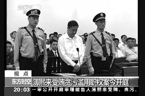 Tidigare politbyråmedlemmen Bo Xilai står mellan två vakter i Jinans mellandomstol i Shandongprovinsen under första dagen av hans rättegång, den 22 augusti. Bo Xilais rättegång förhandlades fram för att få den avpolitiserad, enligt experter. (Skärdump/Epoch Times)