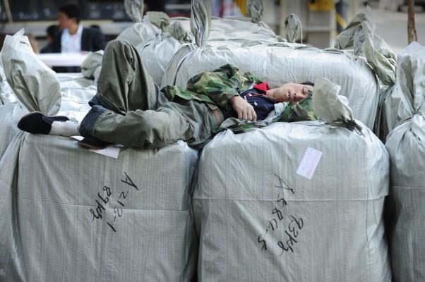En arbetare sover på säckar med varor som skall exporteras i Peking den 14 oktober. (Foto: Peter Parks/AFP)