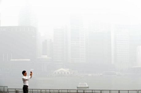 En man tar bilder av byggnader insvepta i smog i Singapore den 19 juni. Luftföroreningsmätaren visade på 152. Branden på Sumatra har orsakat Singapores värsta miljökris på mer än ett decennium. (Foto: Roslan Rahman/AFP)
