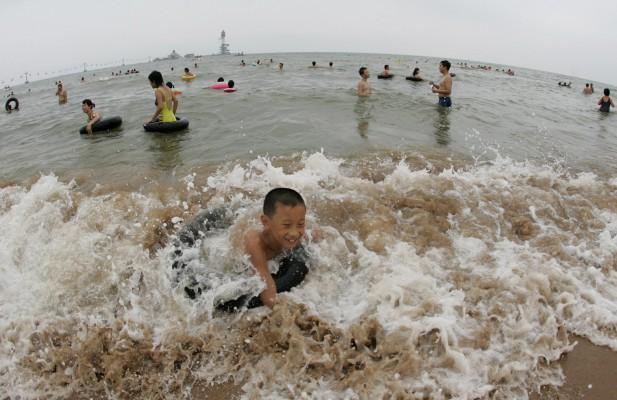 Badande vid Qinhuangdaos strand i Bohaisjön - en kuststad i Kinas nordöstra Hebeiprovins. Kinas exploderande ekonomi har inneburit förstörelse av landets kustområden. Avloppen rinner ofta rätt ut i havet, även på populära turistplatser. (Foto: AFP)