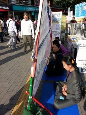 Falun Gong-utövare mediterar på sin informationsplats vid Star Ferry i Hongkong den 13 februari 2013. En rad banderoller som sattes upp av Hong Kong Youth Care Association skymde utövarnas plats. De räfflade plattorna under banderollerna är avsedda för blinda. (Foto: Epoch Times)
