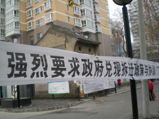 300 vräkningsoffer från samhället Renjiazhuang, Shanxiprovinsen, satte upp banderoller utanför myndigheternas byggnad den 9 december. De säger att de fått löften men lurats av myndigheterna att ge upp sin hus; de nya bostäderna är mycket mindre och kvaliteten är också dålig. (Bild från en av källorna i artikeln)