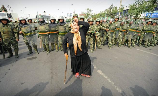 Kravallpolisen står bakom en ensam uigurkvinna i Urumqi, Xinjiangprovinsen den 7 juli, den tredje dagen efter blodbadet. Myndigheterna har beordrat utegångsförbud, och tusentals kraftigt beväpnade poliser skickades till staden Urumqi. (Foton: Peter Parks/AFP)
