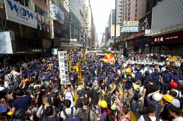 Polis skingrar folk från demonstrationsplatsen i Mong Kok. En demonstrant i vit t-shirt håller upp ett plakat där det står att man kräver att myndigheterna tar tillbaka Nationella folkkongressens beslut om Hongkongs allmänna val, den 26 november 2014. (C.S. Poon/Epoch Times) 