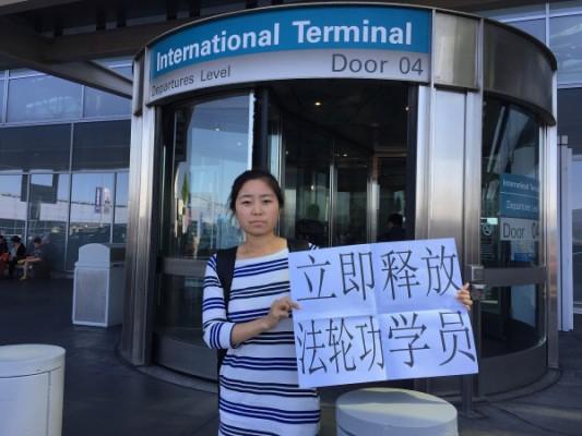 Zhao Guixin, dotter till en av de fängslade Falun Gong-utövarna i Thailand håller upp en skylt utanför San Fransiscos flygplats den 23 april 2015. (Foto: Zhao Guixin)

