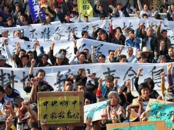 Bybor håller upp banderoller under ett protestmöte i Wukan, i Guanggondprovinsen, den 19 december 2011. Man krävde att myndigheterna skulle agera mot illegala markövertaganden och en lokal ledares död i polisförvar. Ett drygt år senare säger byborna att man inte är nöjda med hur saker har utvecklat sig. (Foto: STR/AFP/Getty Images)