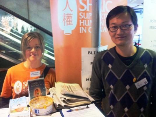 SCRIC:s ordförande Petra Lindberg, här i montern på MR-dagarna i Stockholm, tillsammans med Falun Gong-utövaren Zheng Lu som för närvarande söker asyl i Sverige på grund av förföljelsen i Kina. Zheng Lu är aktiv inom SHRIC. (SHRIC:s foto)