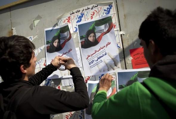 Iranska män hänger upp affischer av en kandidat på en anslagstavla inför parlamentsvalet i centrala Teheran. (Foto: Behrouz Mehri/AFP/ Getty Images)

