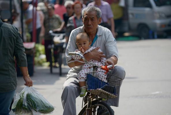 En äldre man håller en bäbis i famnen medan han cyklar på en väg i Kinas huvudstad Peking den 8 september 2015. Kinas befolkning kommer att ha ett ökande antal äldre under de kommande åren, på grund av Kinas ettbarnspolitik. Foto: Wang Zhao/AFP/Getty Images