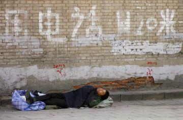 En petitionär sover intill en mur till det som tidigare var en petitionärsby i Peking, men som rivits inför OS. (AFP)