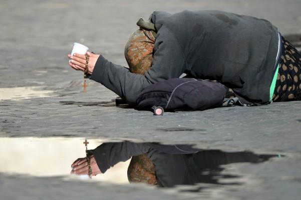 En tiggare ligger på marken på en gata i Rom och ber om pengar medan hon håller i ett radband, den 24 mars 2014. (Gabriel Bouys/AFP/Getty Images)