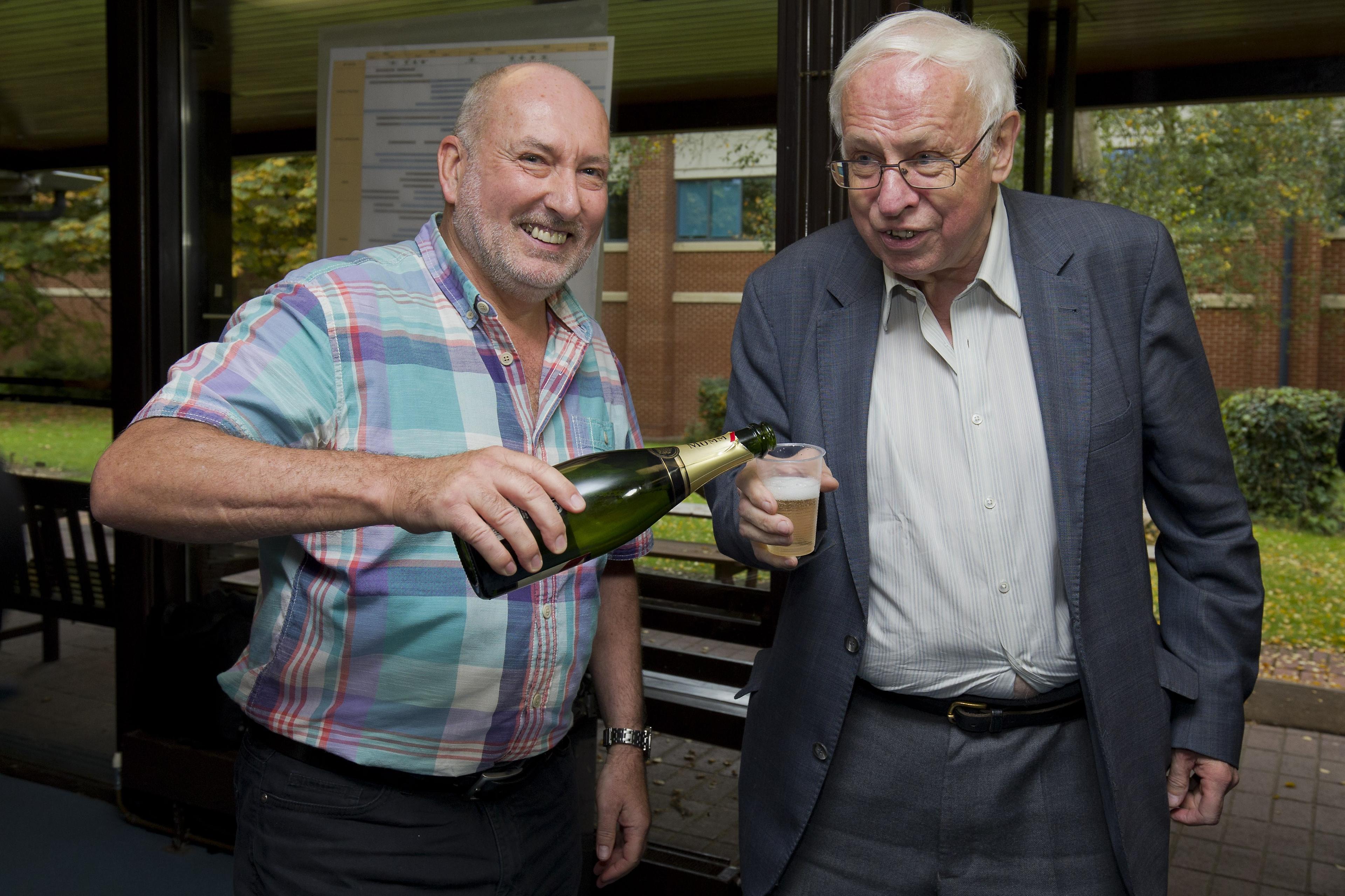 Stephen West (till vänster), biträdande chef på Clare Hall häller upp ett glas champagne till Tomas Lindahl som precis vunnit Nobelpriset i kemi, den 7 oktober 2015. (Foto:  Justin Tallis/AFP/Getty Images)