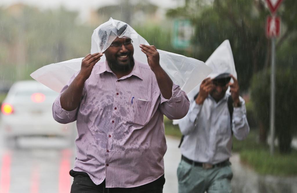 Två män i Dubai använder plastpåsar för att skydda sig mot regnet. (Foto: Kamran Jebreili /AP/TT)