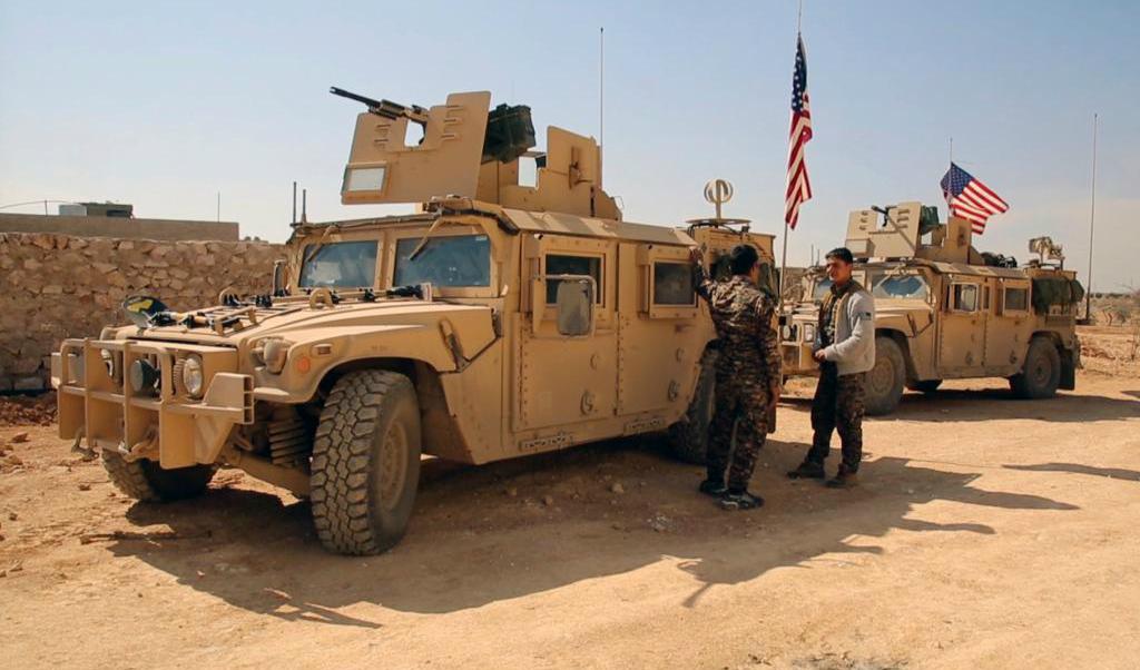 Soldater ur den kurdisk-arabiska alliansen SDF vid några amerikanska militärfordon i norra Syrien. Foto: Arab 24 via AP-arkivbild