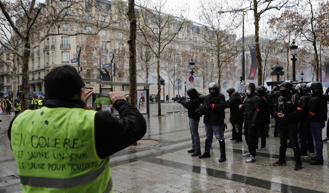 En demonstrant från proteströrelsen Gula västarna tar en bild av kravallpoliser på paradgatan Champs-Élysées i Paris på lördagen. Foto: Kamil Zihnioglu/AP/TT
