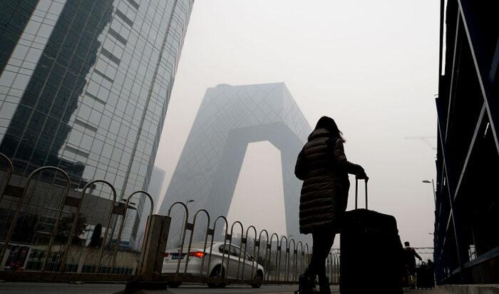En kvinna passerar det nya CCTV-tornet inhöljt i tät smog i Peking den 8 dec. 2015. Foto: STR/AFP via Getty Images.