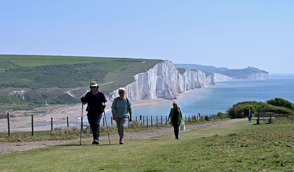 Några människor promenerar på en vandringsled, nära Eastbourne, med Engelska kanalen och Dovers vita klippor i bakgrunden. Klipporna är upp till 106 meter höga och bildades för 135 miljoner år sedan, då var Sverige och Polen täckta av tropiska hav. Foto: Glyn Kirk/AFP via Getty Images