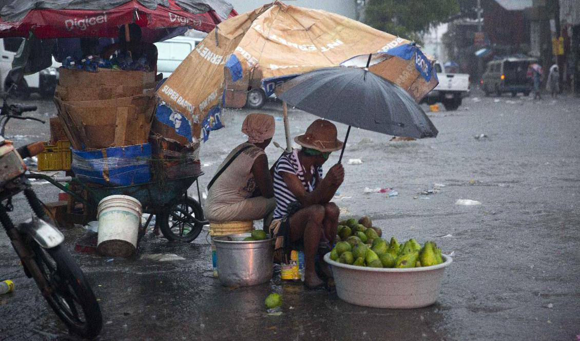 Gatuförsäljare kurar under den tropiska stormen Laura i Port-au-Prince i Haiti på söndagen. Foto: Dieu Nalio Chery/AP/TT