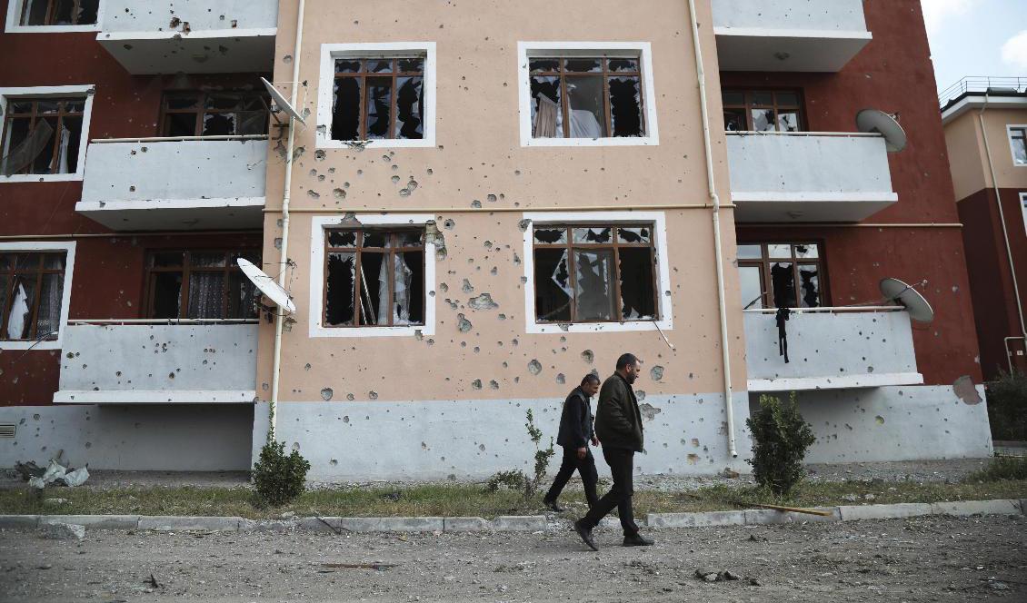 Två män passerar en husfasad märkt av de senaste veckornas strider i Terter i Azerbajdjzan. Bilden är från i lördags. Foto: Aziz Karimov/AP/TT