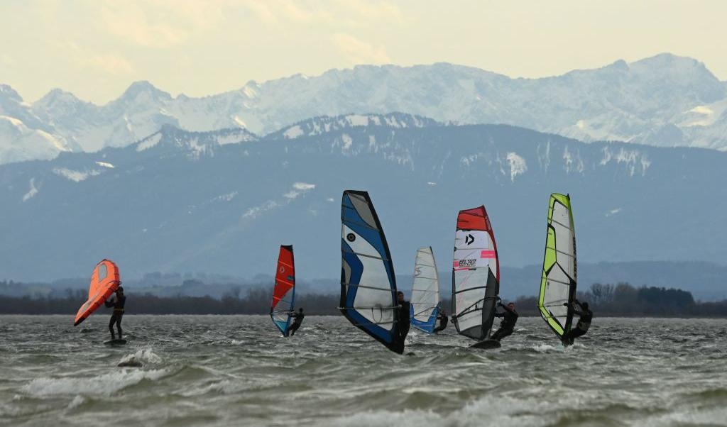 Surfare är ute på sjön Ammersee nära Herrsching i södra Tyskland, en blåsig dag den 13 mars. Bergen i Alperna syns i bakgrunden. Foto: Christof Stache/AFP via Getty Images