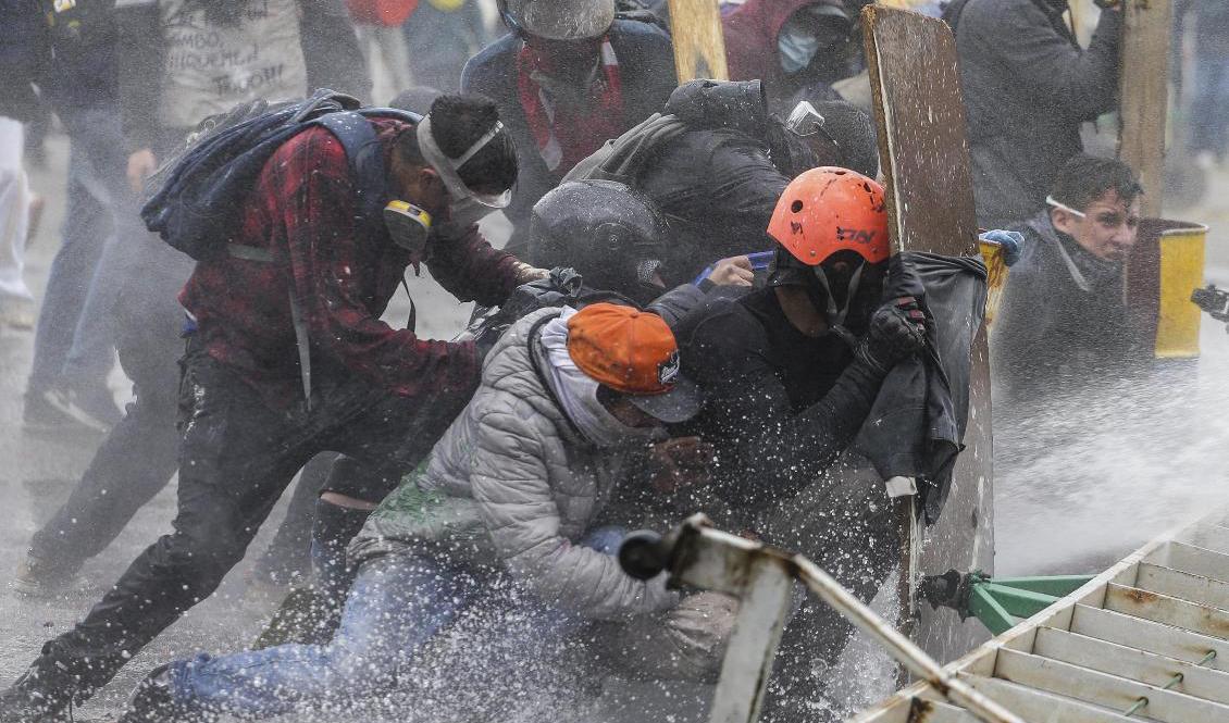 Demonstranter tar skydd från polisens vattenkanoner utanför Colombias huvudstad Bogotá under fredagen. Foto: Ivan Valencia/AP/TT
