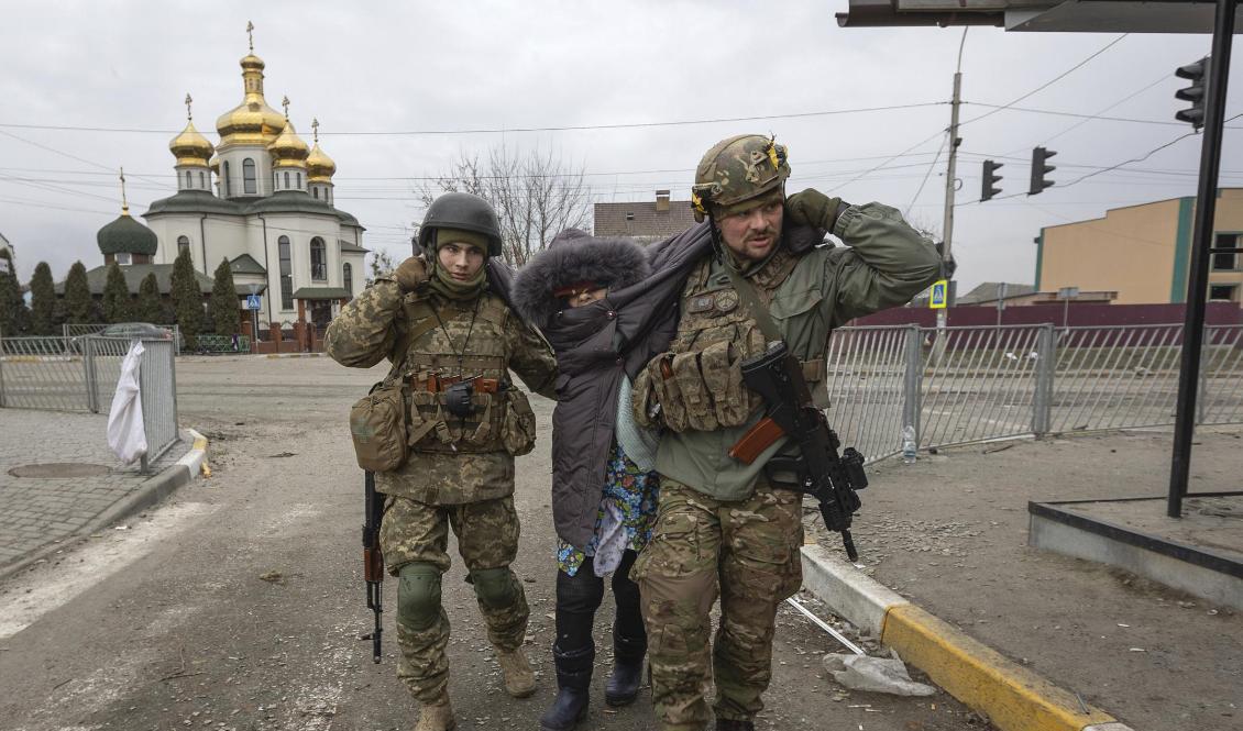 Ukrainska soldater hjälper en kvinna i staden Irpin söndag den 6 mars. Foto: Andriy Dubchak/AP/TT