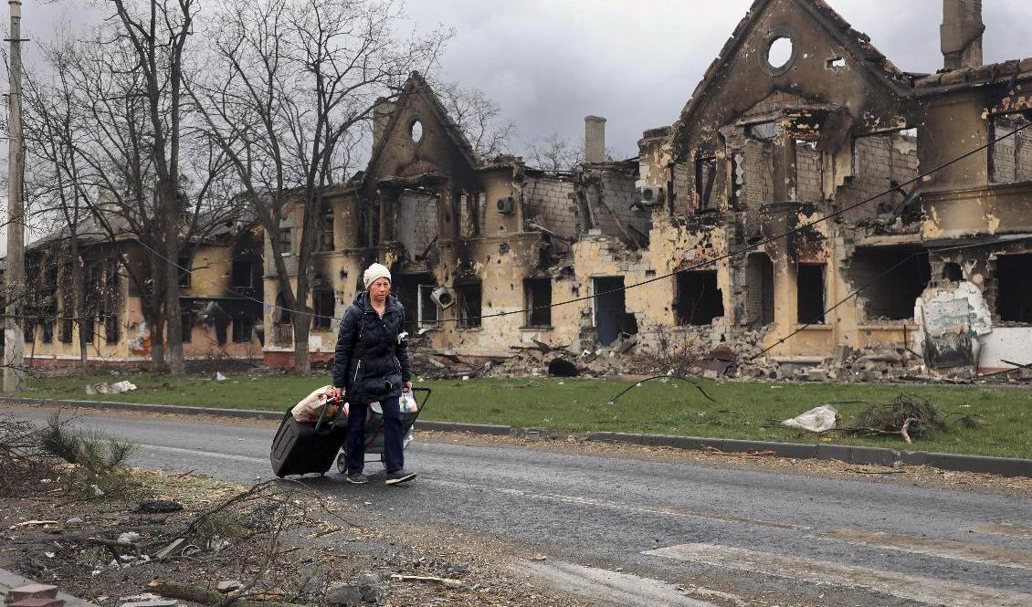 En kvinna drar sin packning förbi skadade hus i Mariupol. Arkivbild. Foto: Alexei Alexandrov/AP/TT