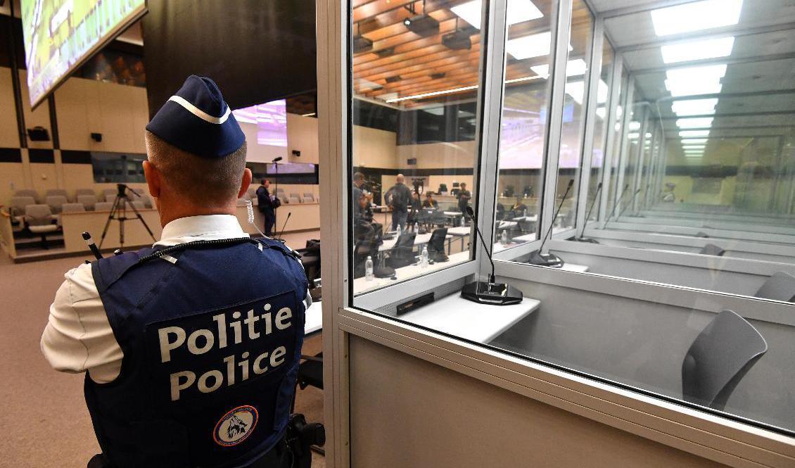 En polis vaktar intill båsen för de anklagade i den rättssal där rättegången kring terrordåden i Bryssel den 22 mars 2016 nu inleds. Foto: John Thys/AP/TT
