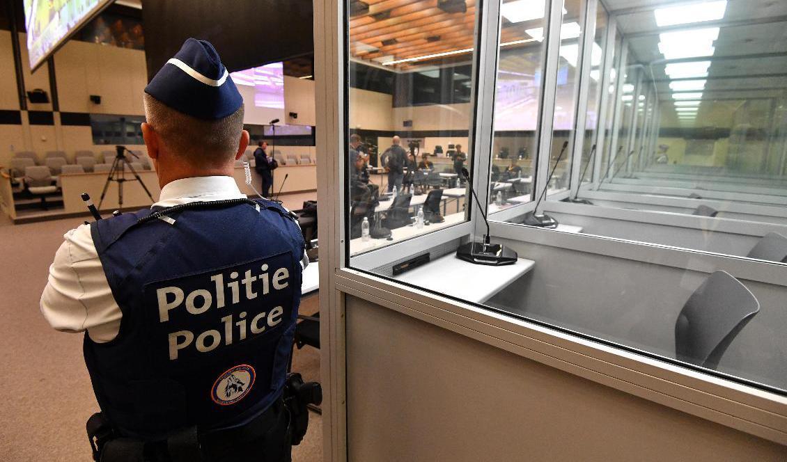 En polisman står invid de glasburar för anklagade i terrorrättegången i Bryssel. Glasburarna byts efter klagomål från försvaret ut och nu har rättegångsstarten försenats flera veckor. Arkivbild. Foto: John Thys/AP/TT