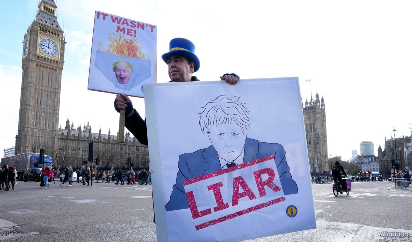 En demonstrant håller upp ett plakat utanför parlamentet i London, där tidigare premiärministern Boris Johnson fick svara på anklagelser om att han vilselett parlamentet angående sin kännedom om brott mot pandemilagarna. Arkivbild. Foto: Kirsty Wigglesworth/AP/TT