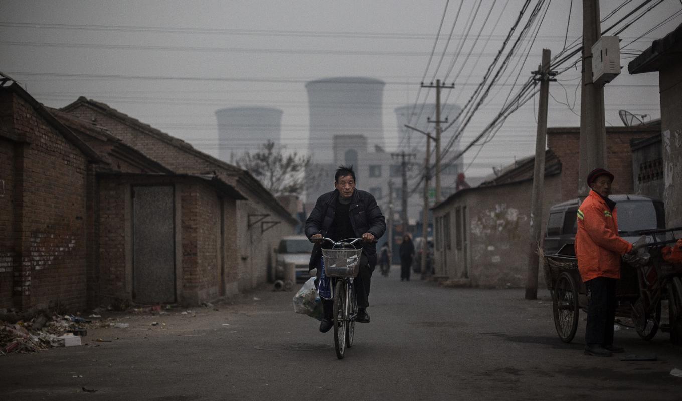 Kina har världens största energisektor. Man använder också mer kolkraft än hela den övriga världen tillsammans. På bilden cyklar en man i Pekings fattiga delar med ett av landets många kolkraftverk i bakgrunden. Foto: Kevin Frayer/Getty Images
