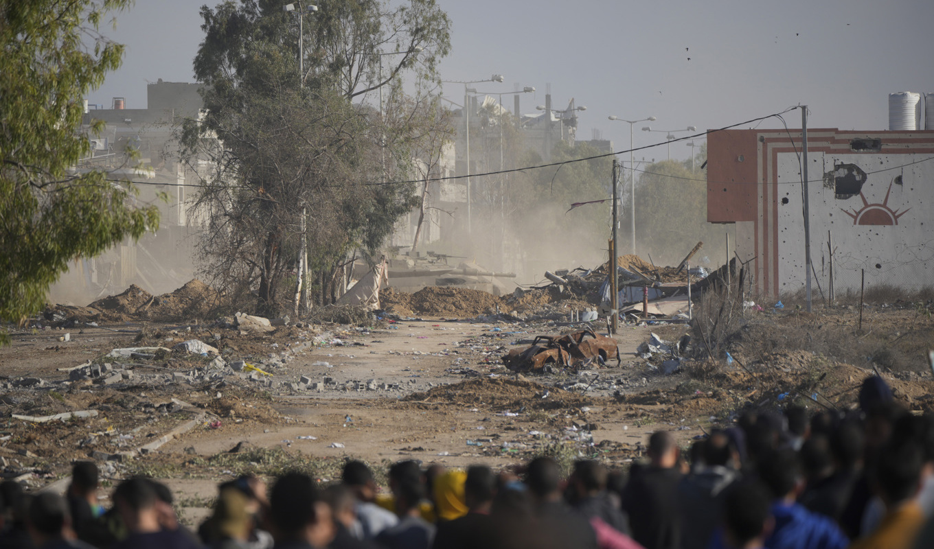 Palestinier tittar bort mot en israelisk stridsvagn som på fredagen blockerar Saladinvägen, den enda större genomfartsleden mellan södra och norra Gazaremsan. Foto: Hatim Mussa/AP/TT
