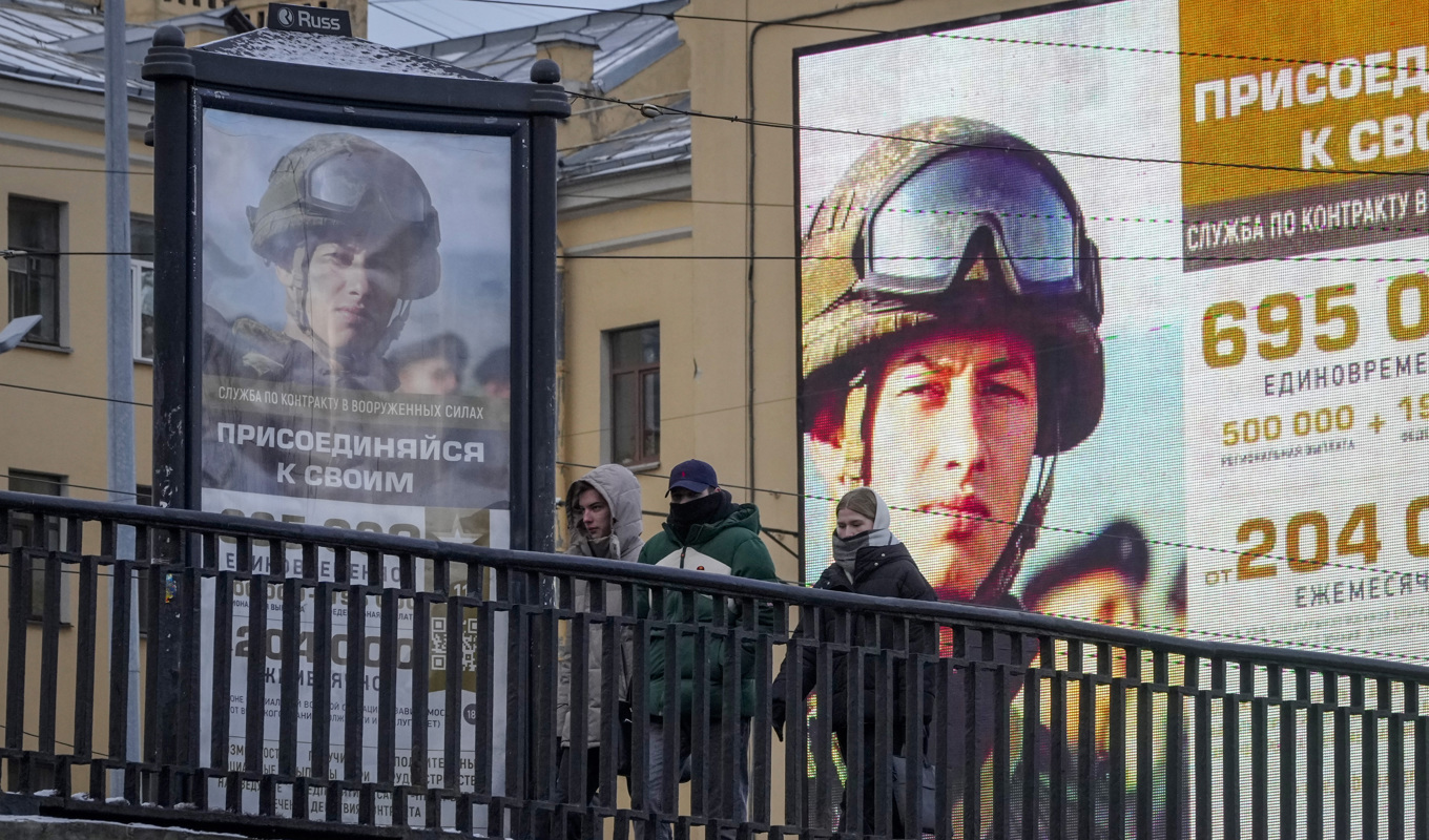 Några unga personer i S:t Petersburg promenerar förbi reklamtavlor där de uppmanas ta värvning i armén. Bilden togs den 22 november. Foto: Dmitri Lovetsky/AP/TT
