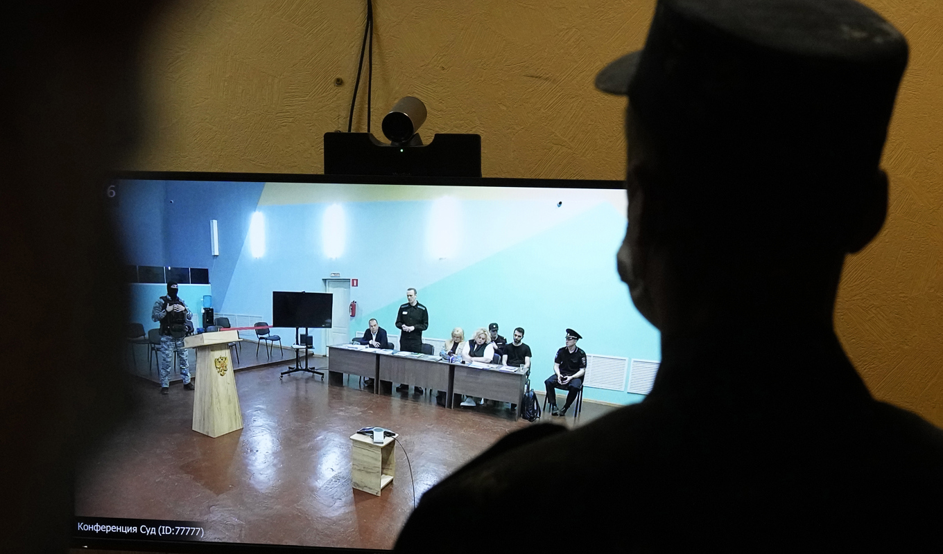 En vakt står framför en tv där Aleksej Navalnyj syns föra sin egen talan i en rättssal i fängelset där han hölls i Melechovo öster om Moskva. Arkivbild från juni i år. Foto: Alexander Zemlianichenko/AP/TT