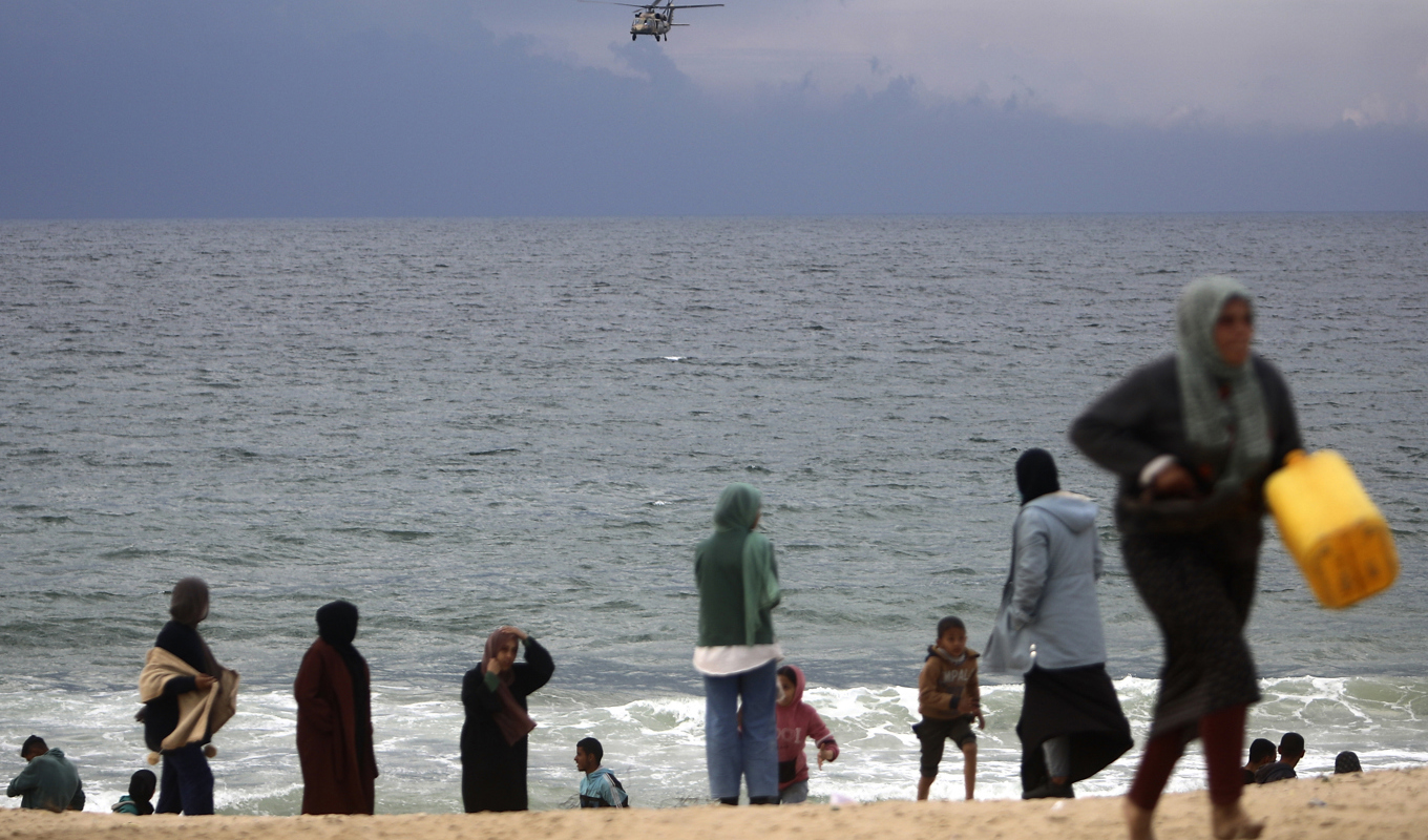 Oroliga palestinier på stranden utanför Khan Yunis tittar ut mot en israelisk militärhelikopter som patrullerar Medelhavet. Bild från i förra veckan. Foto: Mohammad Dahman/AP/TT