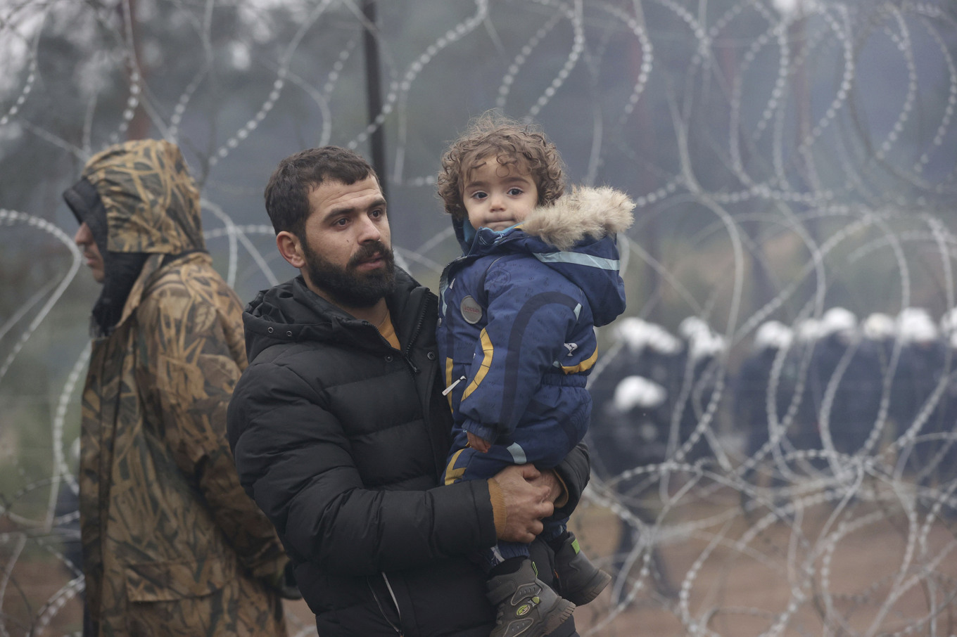 En pappa och hans barn vid taggtrådsstängslet som skiljer Belarus från EU-landet Polen. De senaste åren har Polen sett en ökning av migranter vid gränsen. Bild tagen i november 2021. Foto: Oksana Manchuk/AP/TT