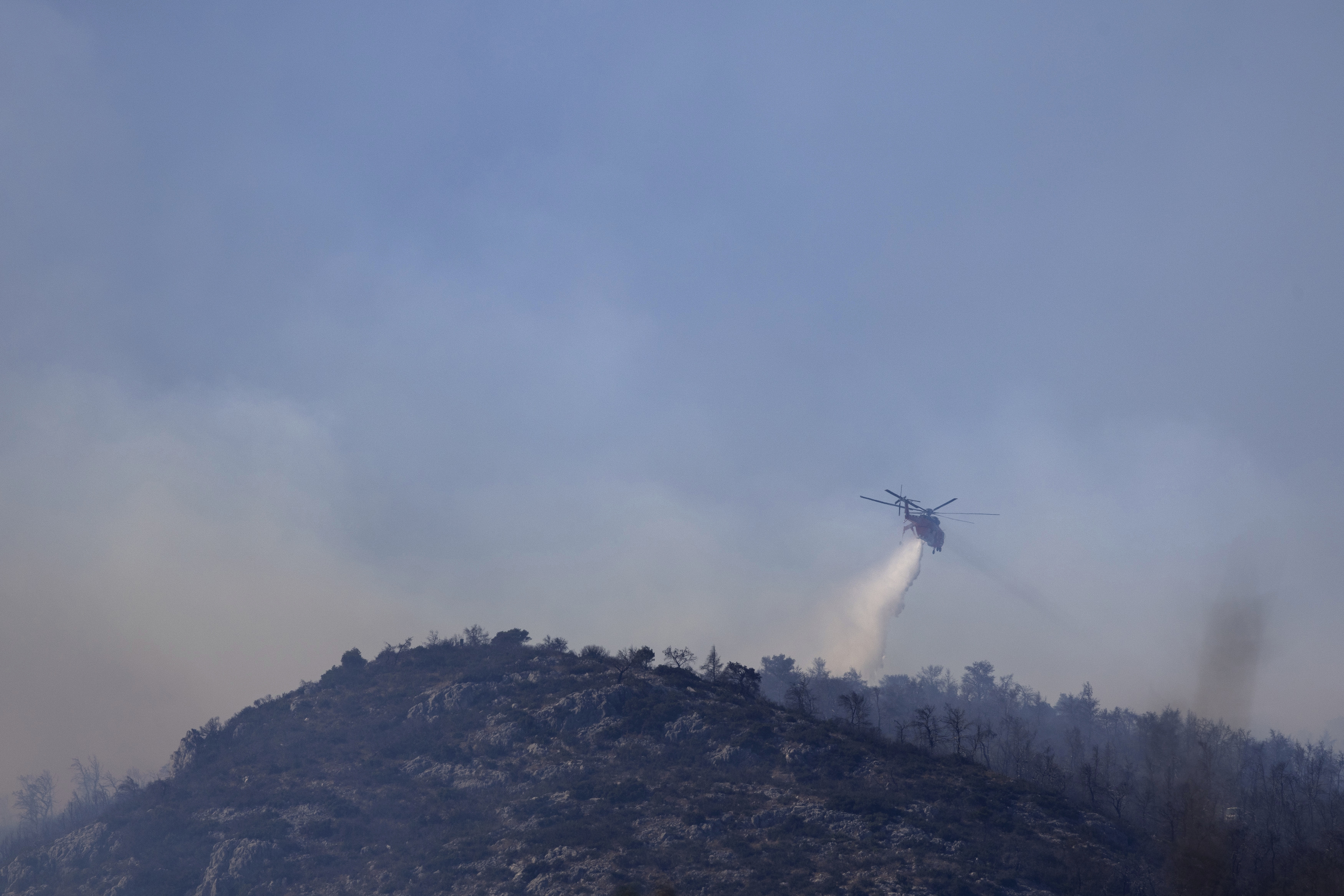 En helikopter som bekämpar en skogsbrand i ett område nordväst om Aten på lördagen. Foto: Yorgos Karahalis/AP/TT