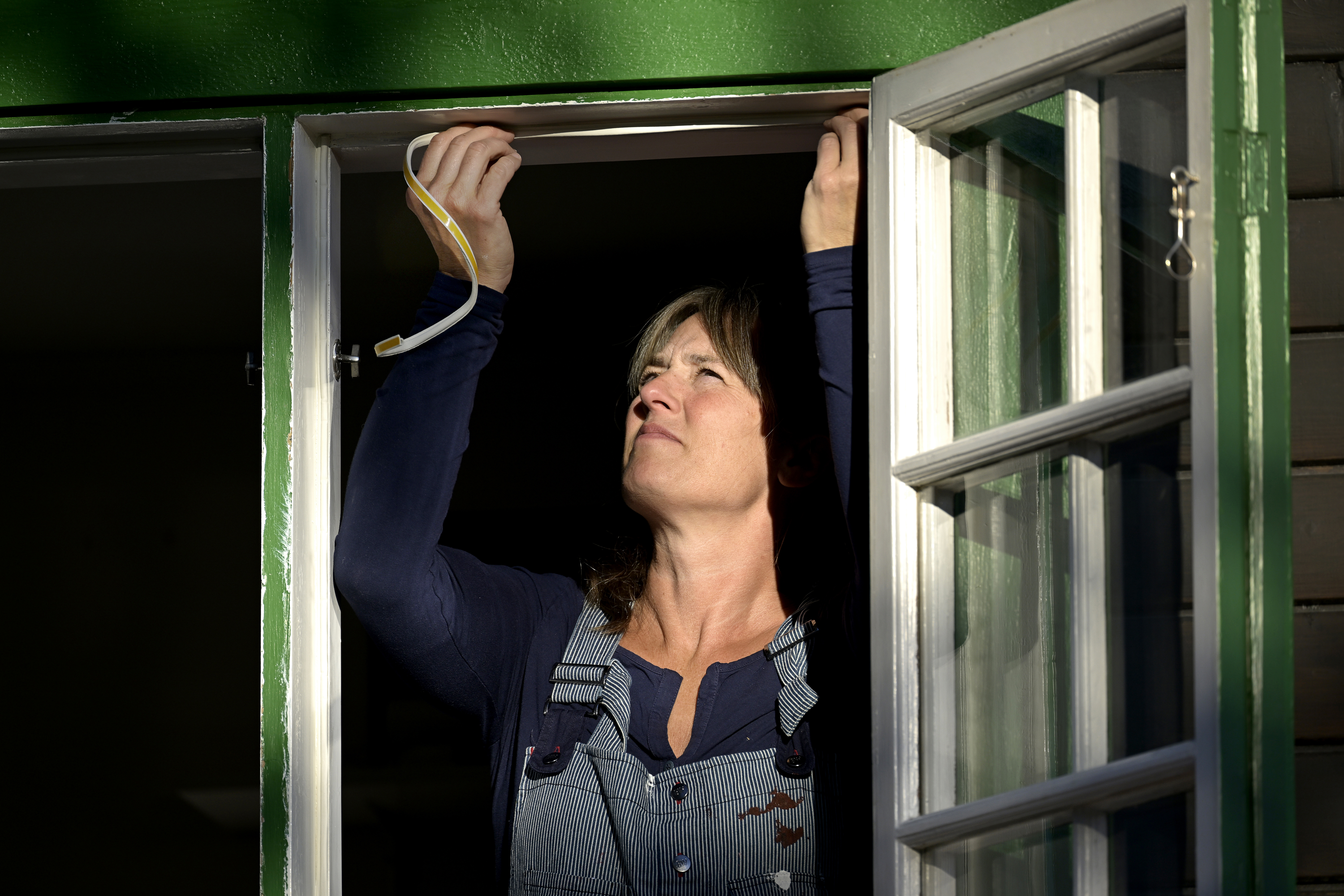 En kvinna sätter upp nya tätningslister till sin bostad, en äldre villa med spröjsade fönster, för att minska drag och spara el och energi inför den kalla årstiden. Foto: Janerik Henriksson/TT