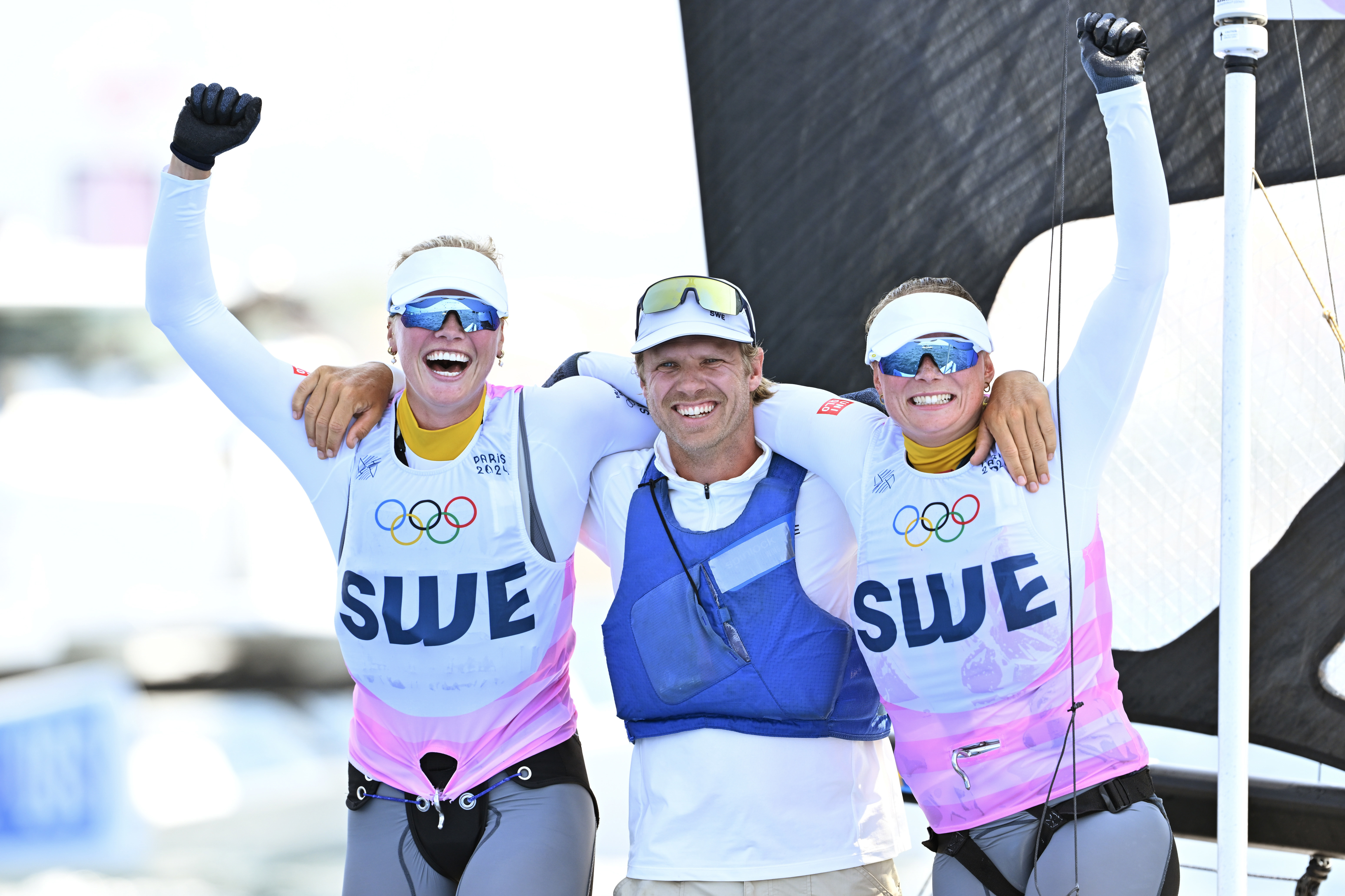 Sveriges Vilma Bobeck och Rebecca Netzler firar OS-silvret i klassen 49erFX med coachen Victor Bergström. Foto: Henrik Montgomery/TT