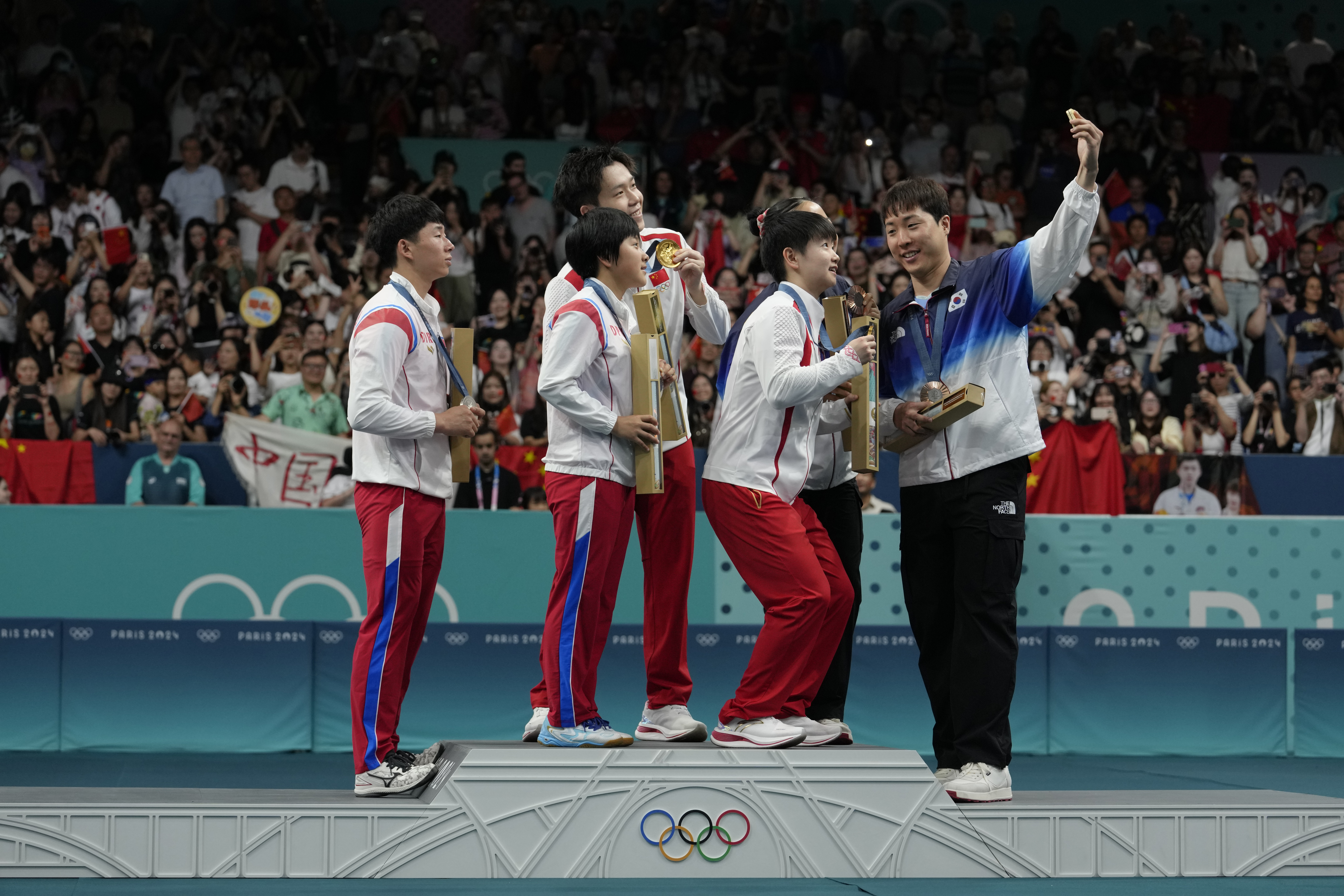 Sydkoreas Lim Jong-Hoon, till höger, tar en selfie med Nordkoreas Ri Jong-Sik, till vänster, Kum Kum-Yong, tvåa från vänster, och övriga på prispallen efter mixedturneringen i Paris. Arkivbild. Foto: Petros Giannakouris/AP/TT