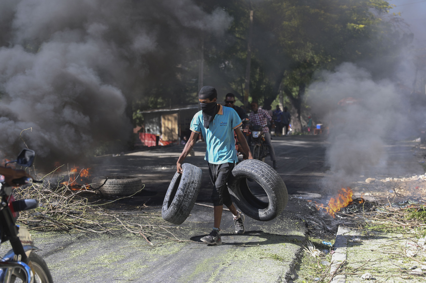 En man bär däck till en brinnande barrikad som ska avskräcka gängmedlemmar från att ta sig in i ett bostadsområde i Port-au-Prince i Haiti. Foto: Odelyn Joseph/AP/TT