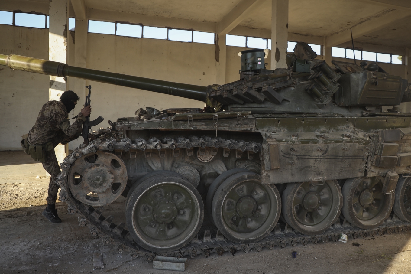 En milisman vid syrisk arméutrustning som övergivits i Maarat al-Numan nära Aleppo på lördagen. Foto: Omar Albam/AP/TT