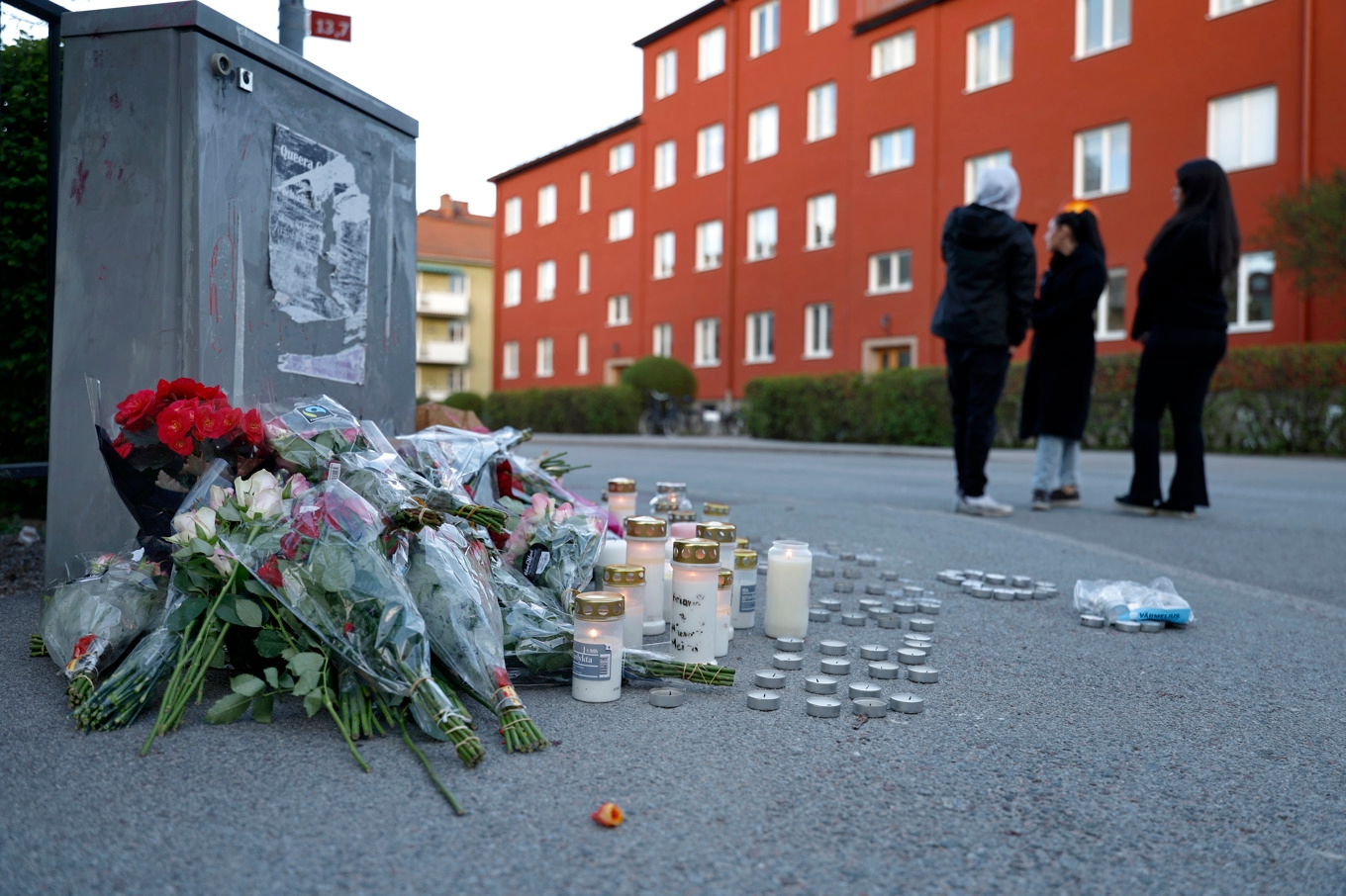 Några personer vid en minnesplats där människor lämnat blommor och ljus dagen efter att tre personer dödats i en skottlossning i en frisörsalong i närheten av Vaksala torg i centrala Uppsala. Foto: Fredrik Persson/TT