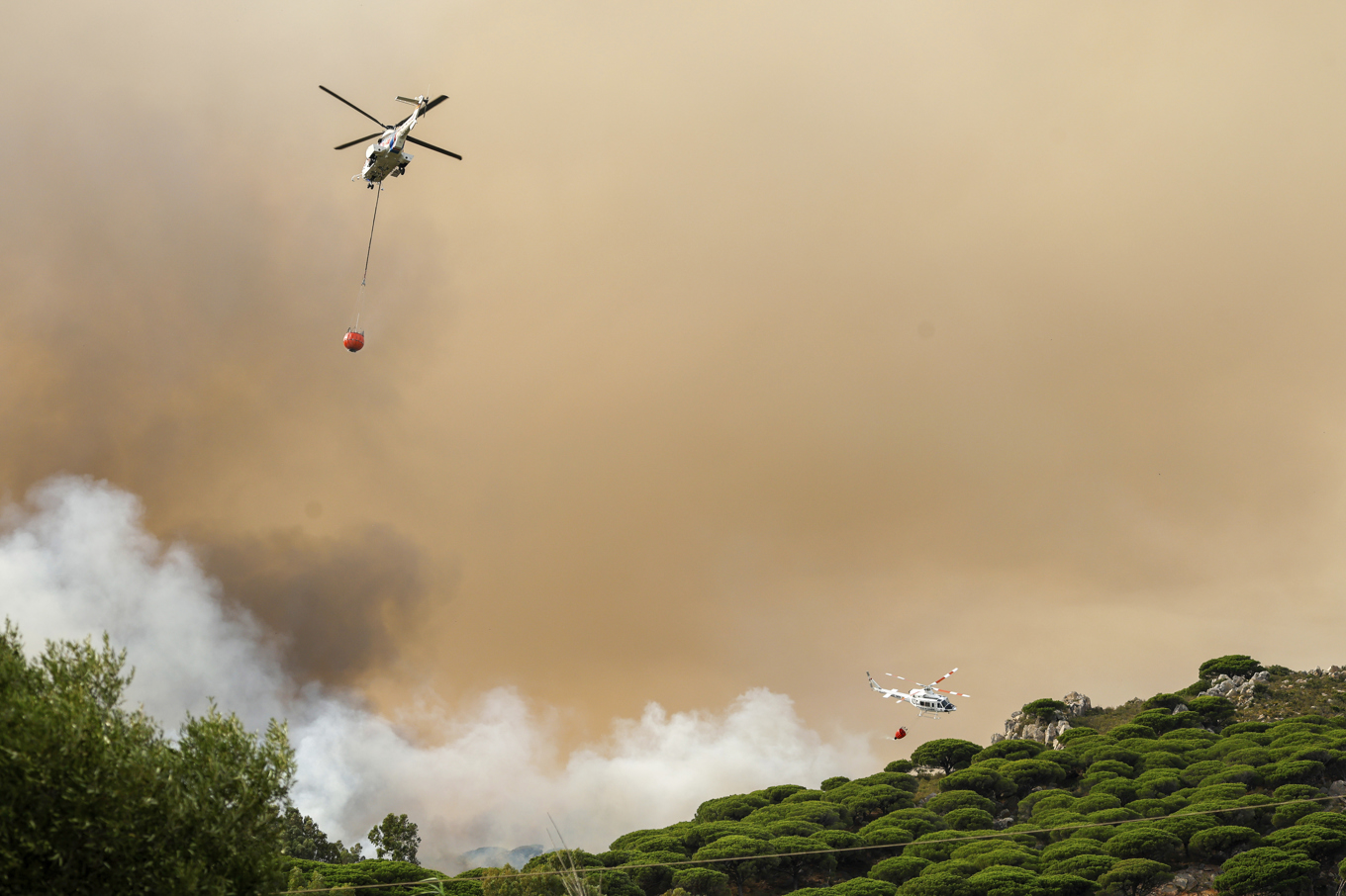 Helikoptrar vattenbombar branden i Torre de la Peña strax utanför turiststaden Tarifa i södra Spanien. Foto: Nono Rico/Europa Press via AP/TT